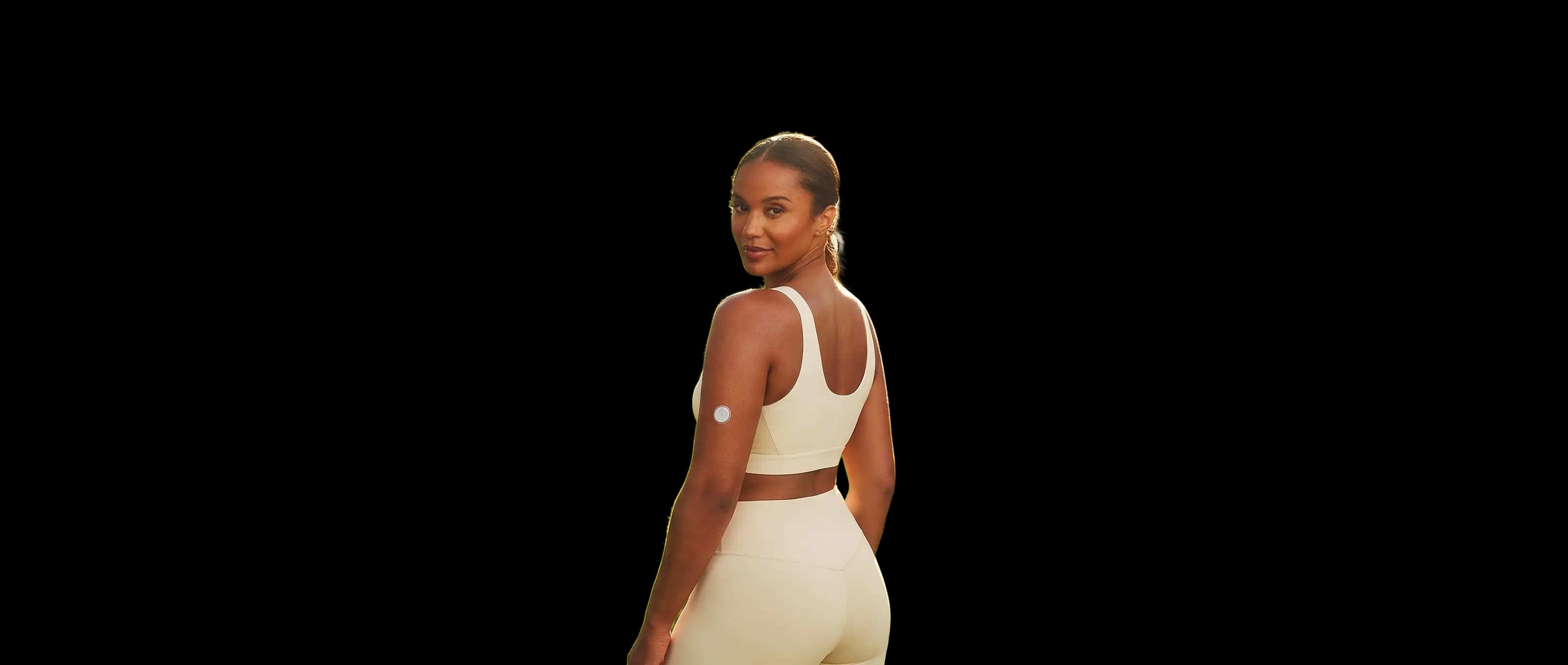 Woman in a sunlit park wearing a Wren glucose sensor on the back of her upper arm